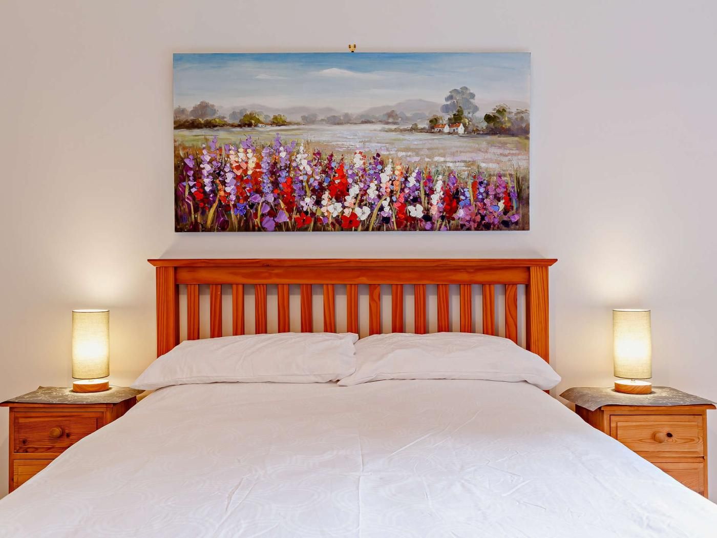 Ein Schlafzimmer mit einem hölzernen Kopfteil, einem Bett mit weißer Bettwäsche, zwei Nachttischen mit Lampen und einem Landschaftsbild über dem Bett.