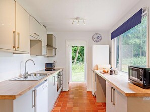 A modern kitchen with white cabinets, a stainless steel sink, a microwave, and a window with a view of greenery. - 2 Bed in Saltash (oc-88312) (Notter)