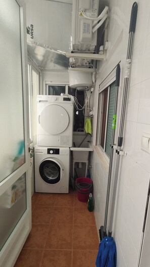 Une petite buanderie équipée d’un lave-linge, d’un sèche-linge, d’un évier et d’un seau.