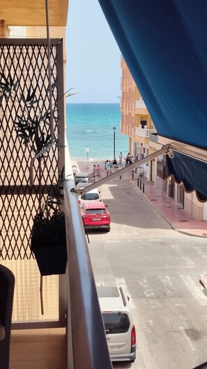A balcony with a view of the sea, a street with parked cars, and buildings with balconies. - La Mata: Beachfront Apartment. 2 bedrooms (La Mata)