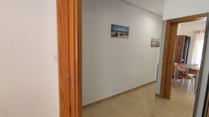 A hallway with a wooden door, a tiled floor, and a dining area with chairs and a table. - La Mata: Beachfront Apartment. 2 bedrooms (La Mata)