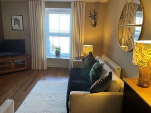 A living room with a sofa, a television, a window with curtains, a wall-mounted deer head decoration, and a lamp. - 1 Bed in Harrogate (oc-88520) (Pateley Bridge)