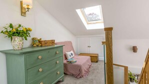 Ein Schlafzimmer mit Oberlicht, einem grünen Schminktisch, einem rosa Bett und einer Holztreppe.