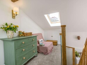 Ein Schlafzimmer mit Oberlicht, einem grünen Schminktisch, einem rosa Bett und einer Holztreppe.