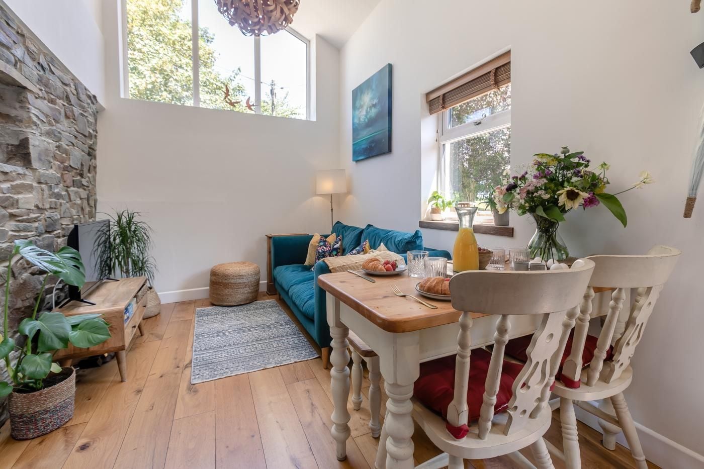 A cozy living room with a stone wall, a blue sofa, a wooden dining table, and a white chair.