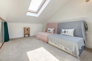Ein Schlafzimmer mit Oberlicht, einem Bett mit gemusterten Betttextilien, einem kleinen Nachttisch aus Holz und einem Teppichboden.