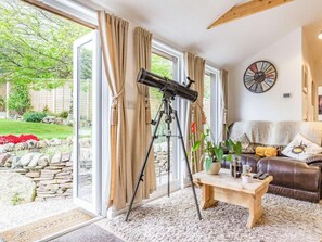A room with a telescope, a sofa, a coffee table, and a view of a garden through a glass door.