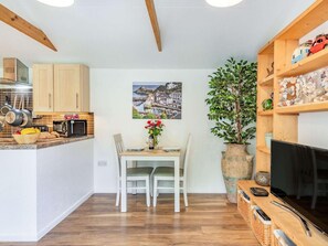 A compact kitchen with wooden cabinets, a dining table with chairs, a potted plant, and a flat-screen TV. - 1 Bed in Bodmin (oc-88049) (Luxulyan)