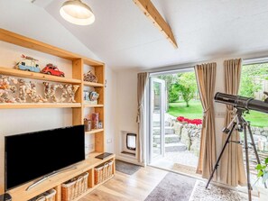 A living room with a television, wooden shelves with various items, a telescope, and a view of a garden through a glass door. - 1 Bed in Bodmin (oc-88049) (Luxulyan)