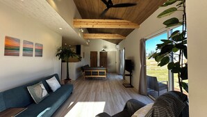 A modern living room with a wooden ceiling, a blue sofa, a dining table, and a large window. - Dog Cottage Surfside Kujukuri (Kujukuri)