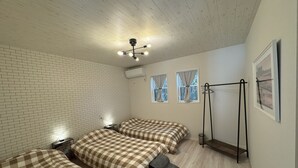 A room with a brick-patterned wall, a bed with a checkered bedspread, a bedside table with a lamp, and a window with curtains. - Dog Cottage Surfside Kujukuri (Kujukuri)