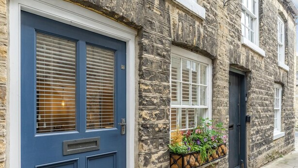 Ein Steinhaus mit einer blauen Tür, einem Fenster mit Blumenkasten und einem kleinen Fenster mit einer schwarzen Tür.