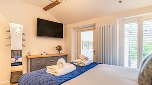 Ein Schlafzimmer mit Bett, Kommode, Fernseher und einem Fenster mit Vorhängen.