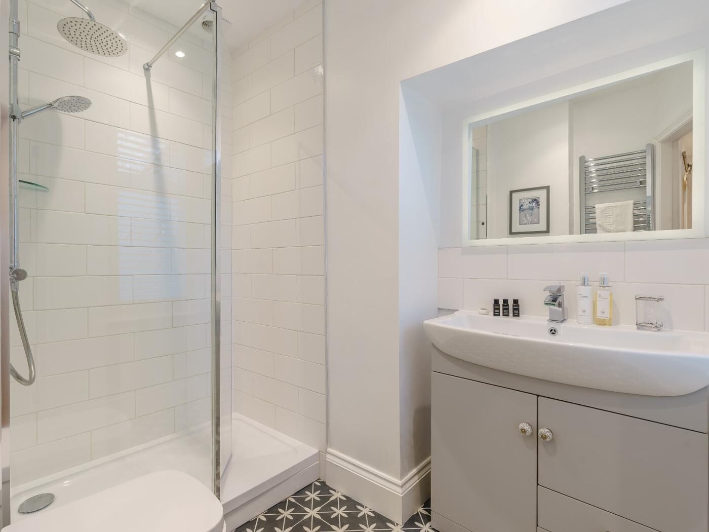 A modern bathroom with a glass-enclosed shower, a white sink with a mirror above, and a tiled floor.