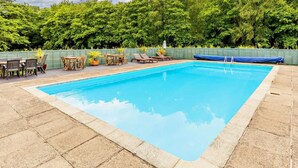 A rectangular swimming pool with a tiled deck, surrounded by a green fence, and a seating area with tables and chairs. - 2 Bed in Saltash (oc-88313) (Notter)