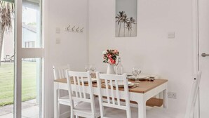 A dining area with a wooden table, white chairs, a vase with flowers, and a wall-mounted picture. - 2 Bed in Saltash (oc-88313) (Notter)