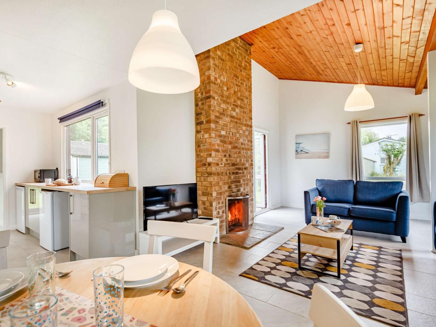 A modern living room with a fireplace, a blue sofa, and a dining area with a table set for two.