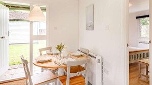 Uma área de refeições com uma mesa redonda, cadeiras brancas, uma luminária pendente e um radiador.