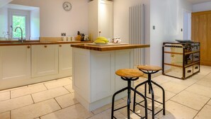A kitchen with a central island, bar stools, a clock, and a radiator. - 2 Bed in Ambleside (oc-88319) (Claife)