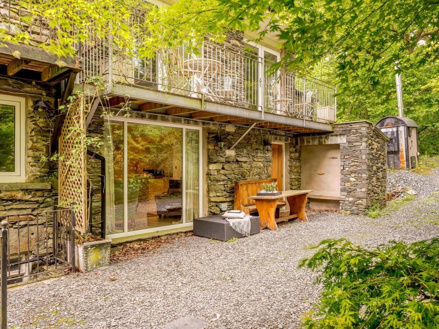 A stone house with a balcony, a wooden bench, and a gravel driveway.