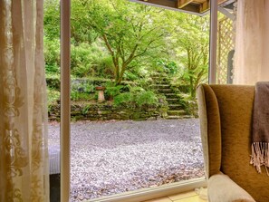 A room with a view of a garden through a window, a stone wall, and a stone staircase.
