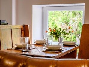 A dining table set with plates, glasses, and a vase with flowers, positioned near a window with a view of greenery.