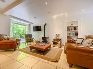 Ein geräumiges Wohnzimmer mit Ledersofas, einem Kamin, einem Bücherregal und einem Fernseher.