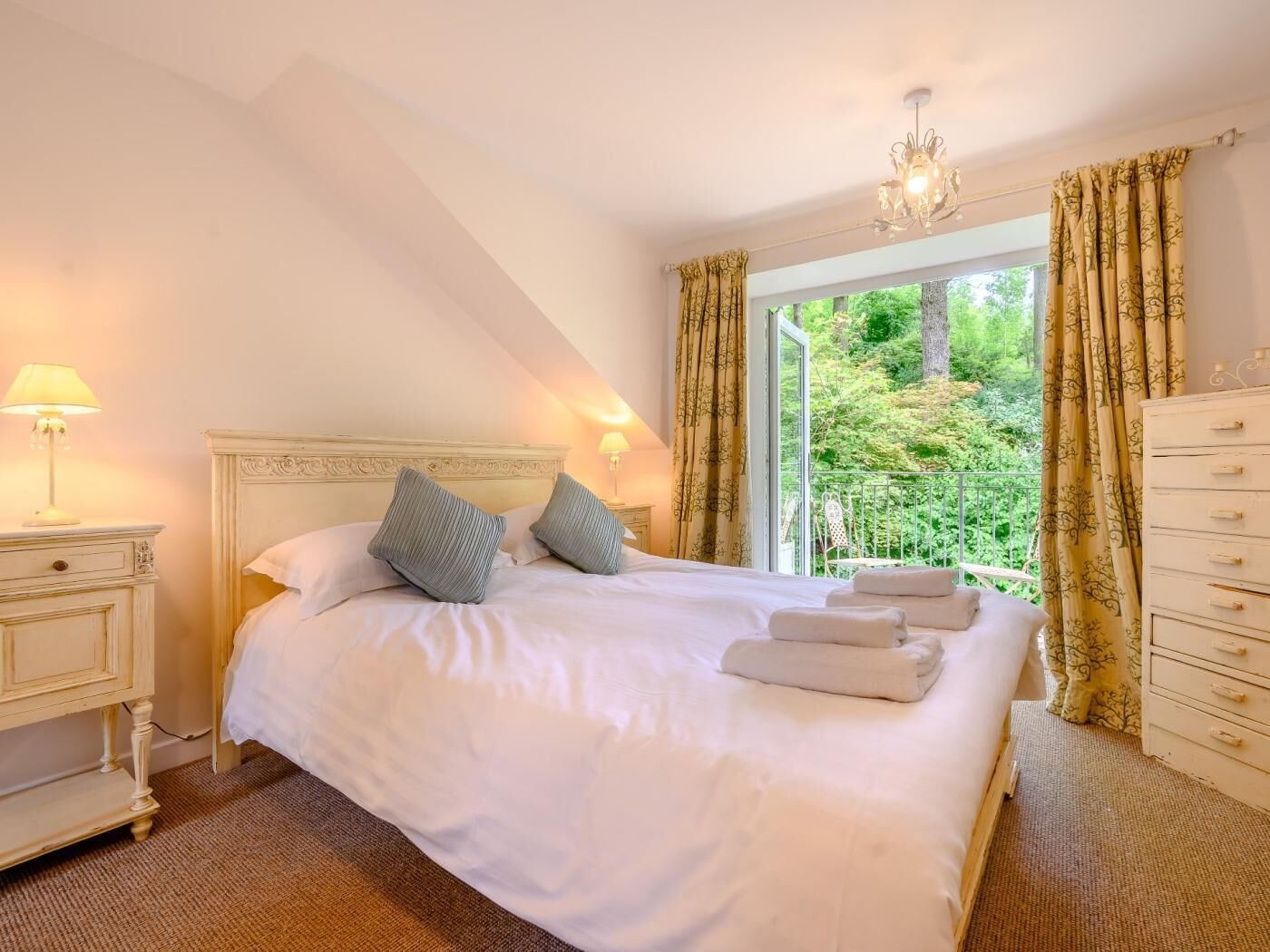 A bedroom with a large bed, a nightstand, a dresser, and a window with curtains.
