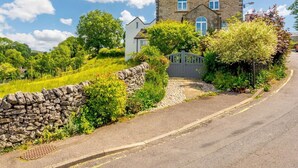 A stone house with a gated entrance, surrounded by lush greenery and a stone wall. - 4 Bed in Buxton (oc-88196) (Hartington)
