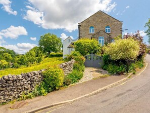 A stone house with a gated entrance, surrounded by lush greenery and a stone wall. - 4 Bed in Buxton (oc-88196) (Hartington)