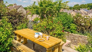 A wooden table with a bench, a stone wall, and a garden with various plants and flowers. - 4 Bed in Buxton (oc-88196) (Hartington)