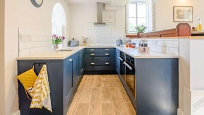 A modern kitchen with a central island, dark blue cabinets, white countertops, and a visible clock on the wall. - 4 Bed in Buxton (oc-88196) (Hartington)