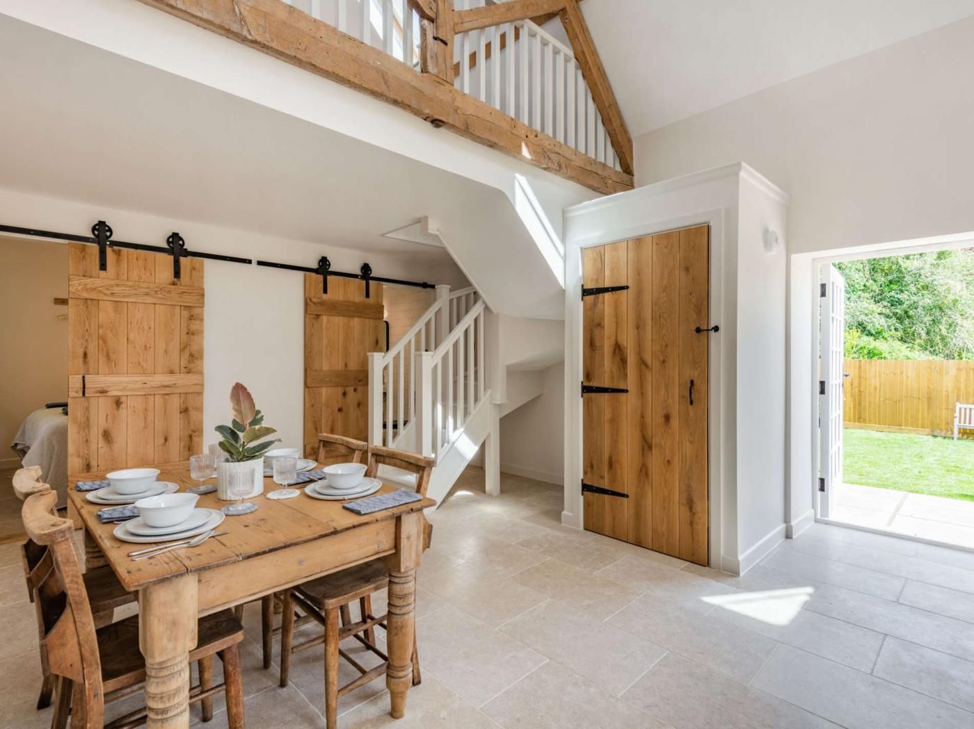 Un coin repas avec une table en bois dressée pour quatre personnes, un escalier et une porte donnant sur l’extérieur.