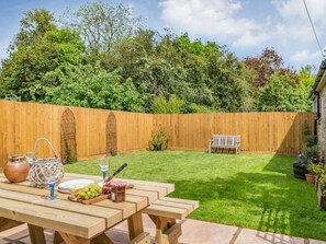 Ein Garten mit Holzzaun, einem Picknicktisch mit Speisen und Getränken und einer Bank.