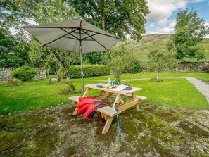 Una mesa de picnic con toldo, rodeada de follaje y un muro de piedra.