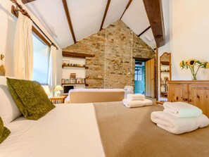 Un dormitorio con pared de piedra, cama con almohadas, mesita de noche con lámpara y vistas al baño.