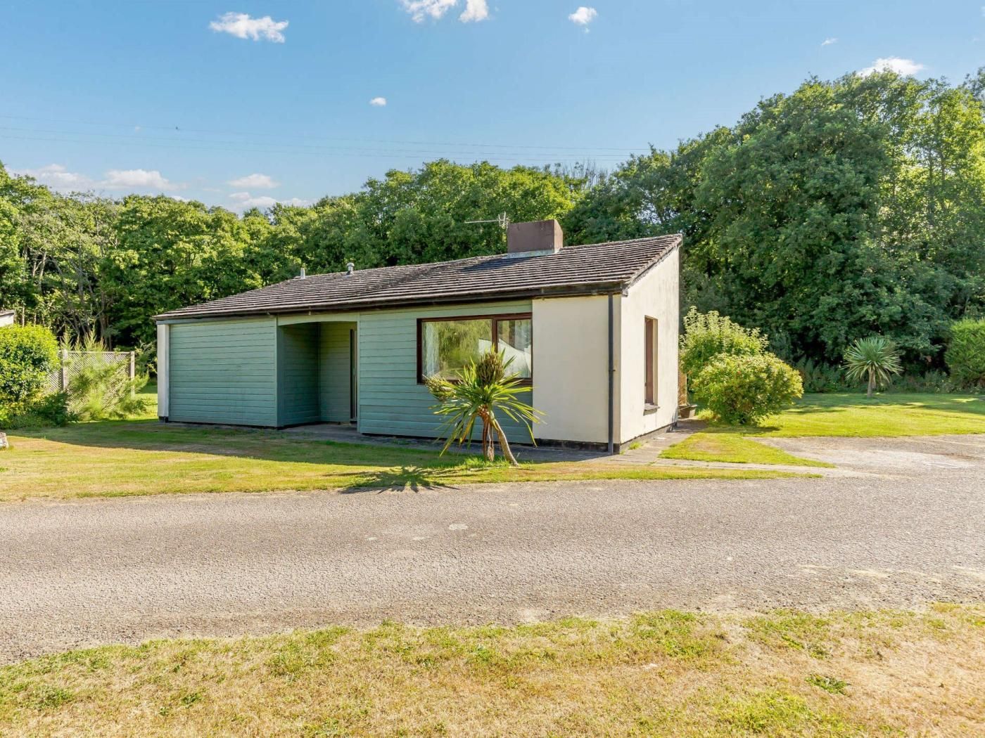 Een klein, laag huis met schuine kap, een voordeur en een klein voortuintje.