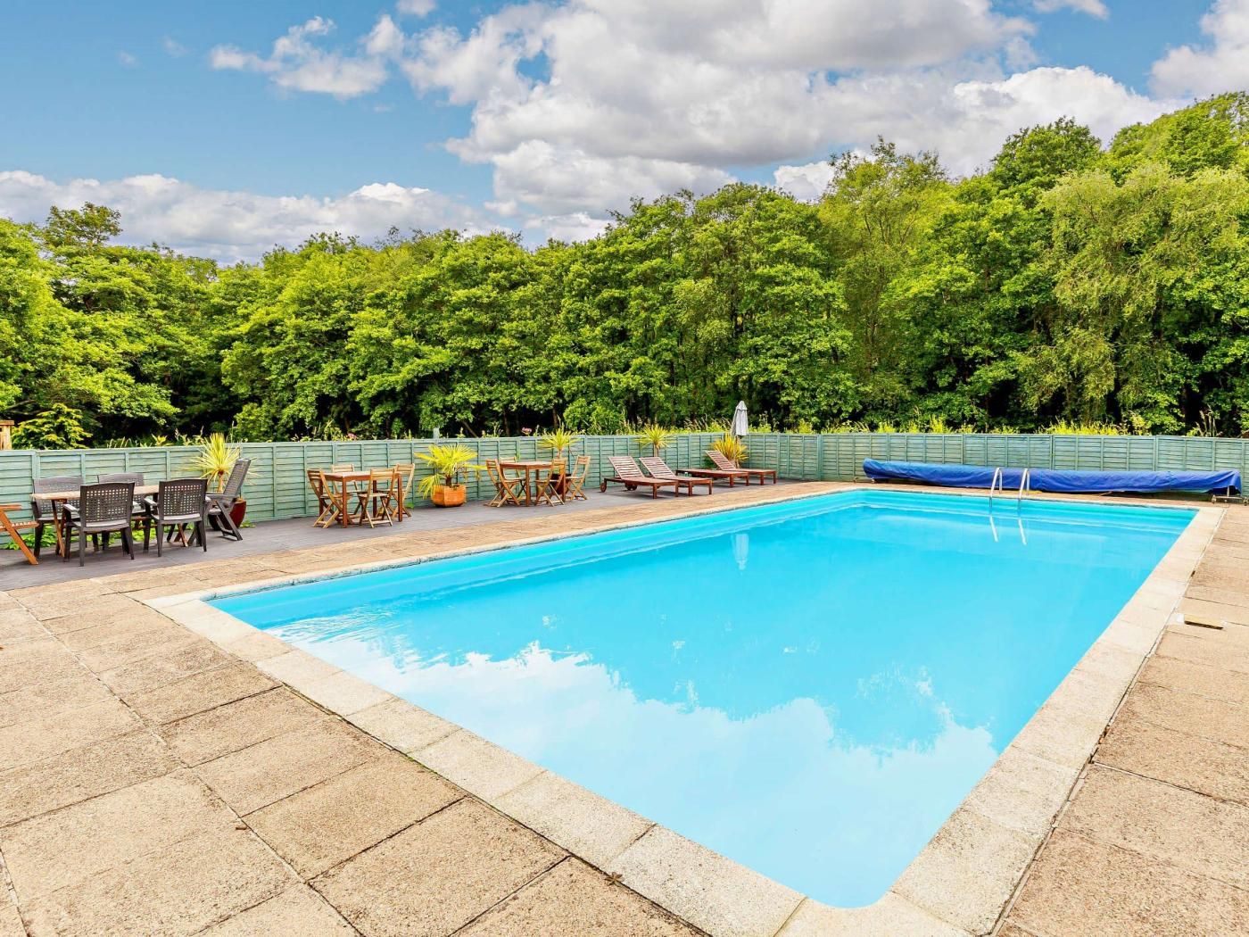 Uma piscina retangular com um espaço de pátio ao redor, incluindo espreguiçadeiras e uma mesa.
