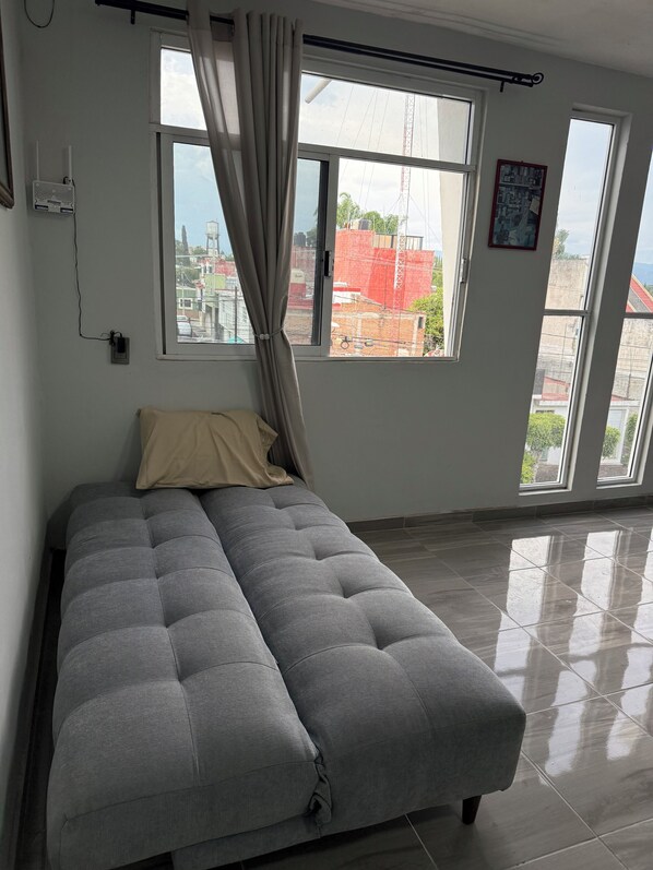A bedroom with a bed, large windows, and a view of buildings outside.