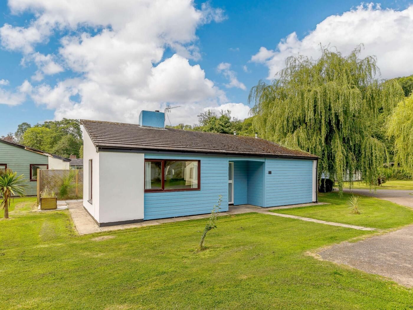 Een gelijkvloers huis met een blauwe gevel, een voordeur en een kleine voortuin.