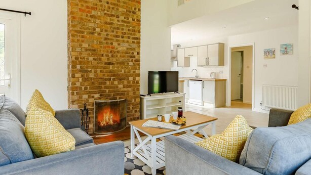 A living room with a brick fireplace, a television, and a kitchen area in the background. - 2 Bed in Saltash (oc-88311) (Notter)