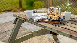 A picnic setup with a wooden table, a plate of scones, two cups, a teapot, and a jug. - 2 Bed in Saltash (oc-88311) (Notter)