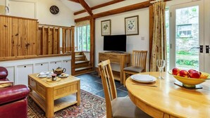 Ein gemütliches Zimmer mit einer Holztreppe, einem Fernseher, einem Esstisch mit Stühlen und einem roten Ledersofa.
