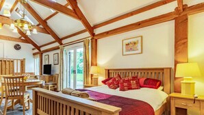 Ein Schlafzimmer mit einem hölzernen Bett, einem Holz-Kopfteil, einem Nachttisch mit Lampe sowie einem Fenster mit Vorhängen.