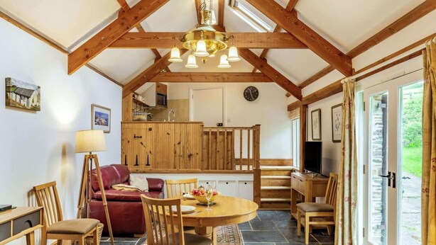 Ein geräumiges Zimmer mit hohen Decken, Holzbalken, einem Essbereich mit rundem Tisch, Stühlen und einem roten Sofa.