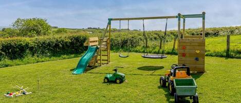 A grassy outdoor play area with a slide, swings, and a climbing structure.