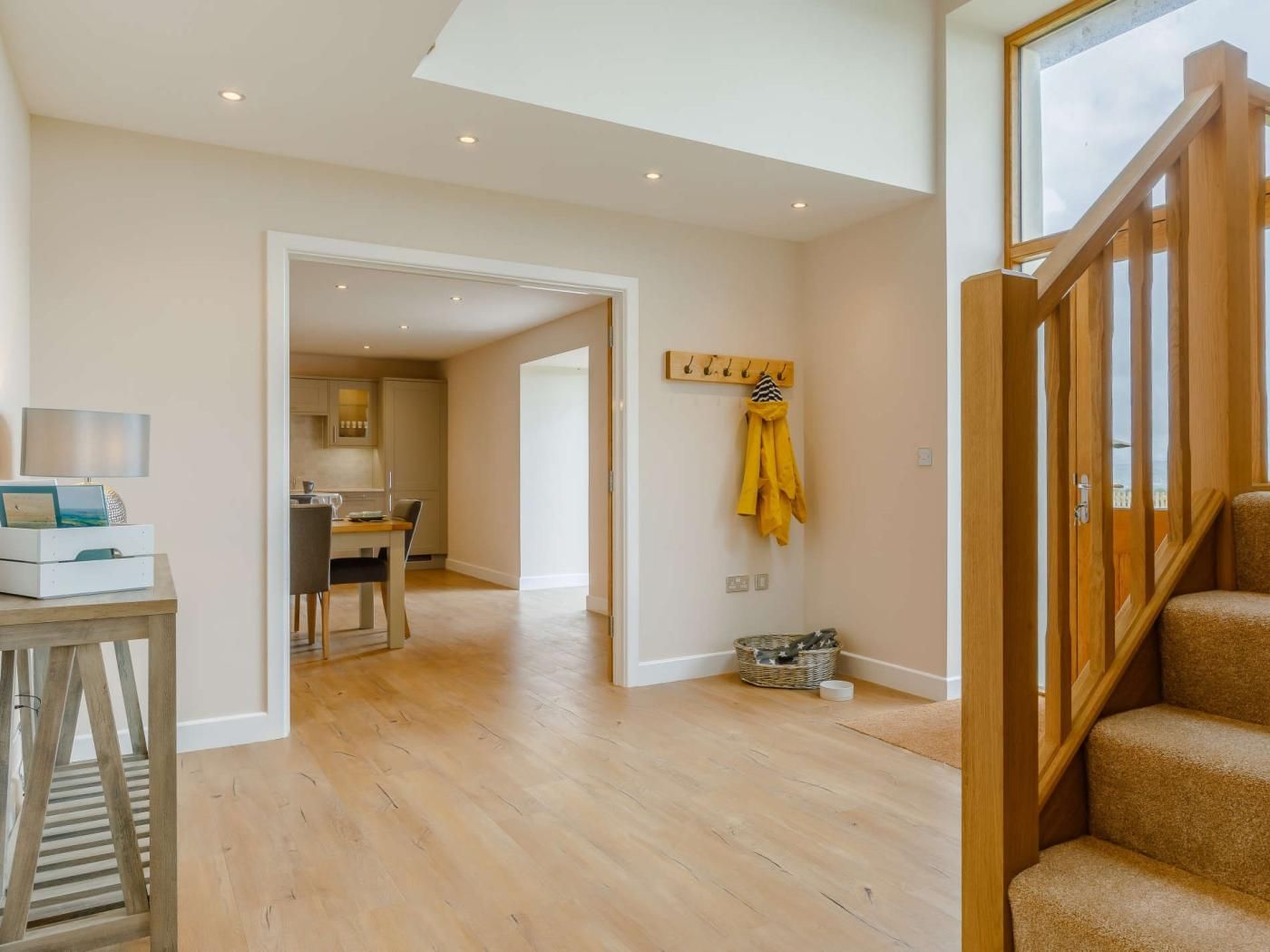 A spacious room with a wooden floor, a dining area with a table and chairs, a coat rack with a yellow jacket, and a staircase with wooden railings.