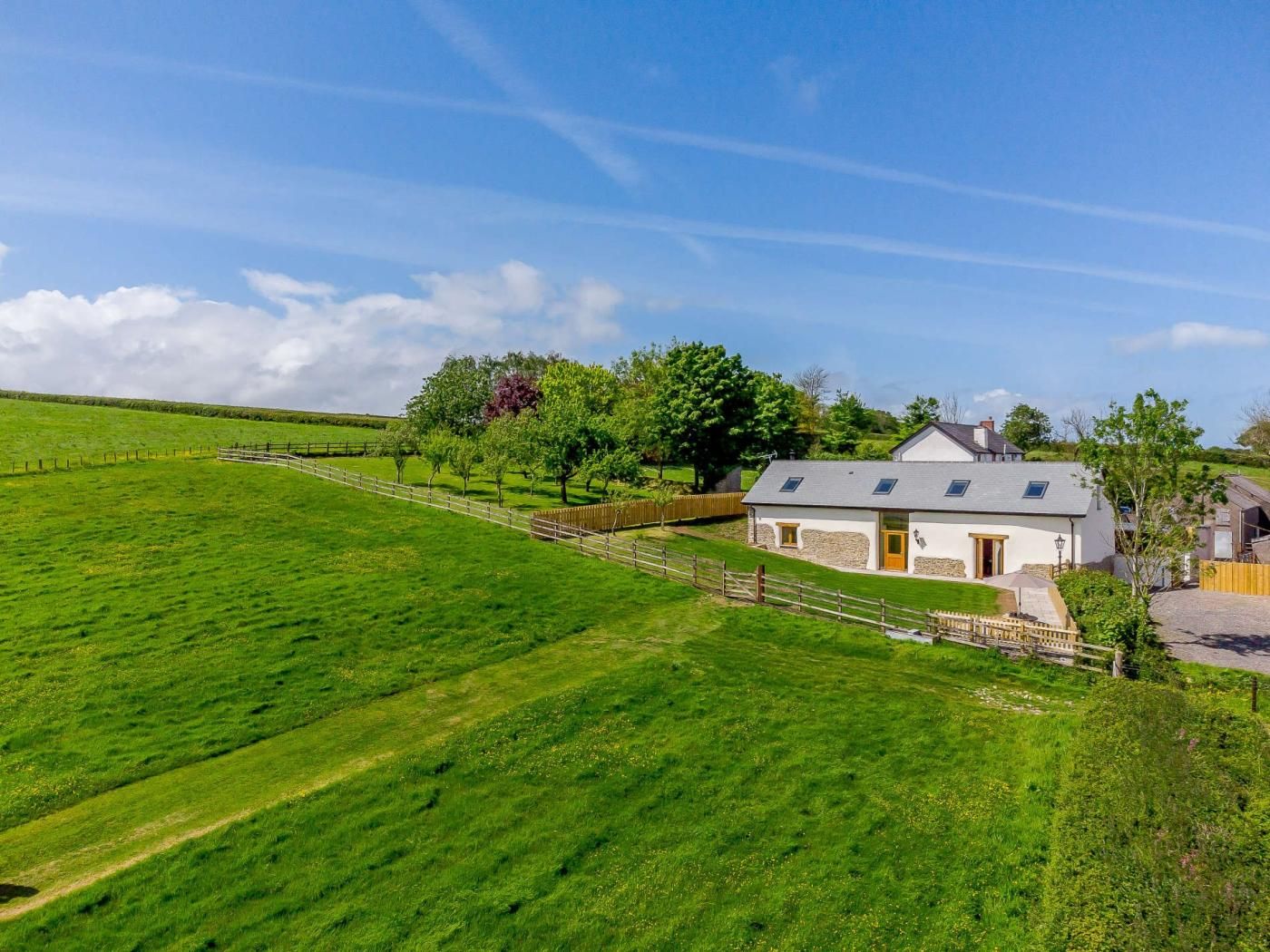 A white house with a stone foundation, a fenced yard, and a clear sky.