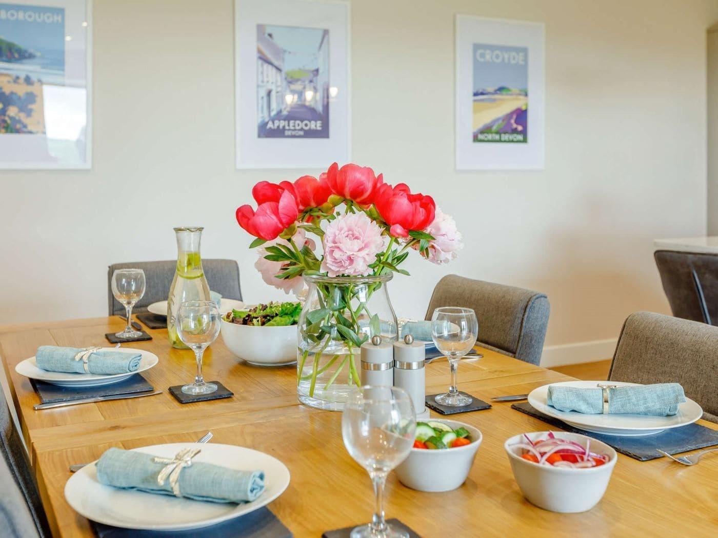 A dining table set with plates, glasses, a vase of flowers, and condiments.