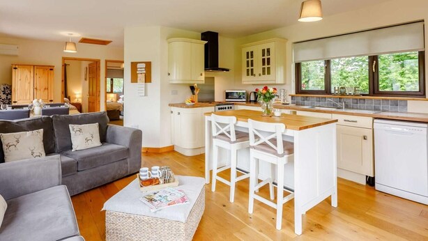 Una cocina moderna con armarios blancos, una isla central con taburetes y una zona de comedor con un sofá gris.
